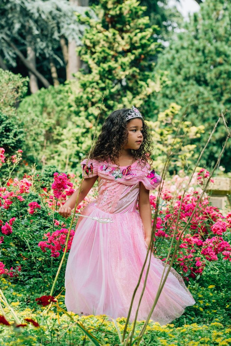 Meisje in een roze prinsessenjurk die rent in de tuin met een toverstaf